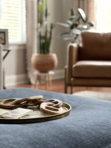 Navy ottoman with a brass styling tray and a tan leather chair beyond, by Hayden Home Studio in Weddington, NC